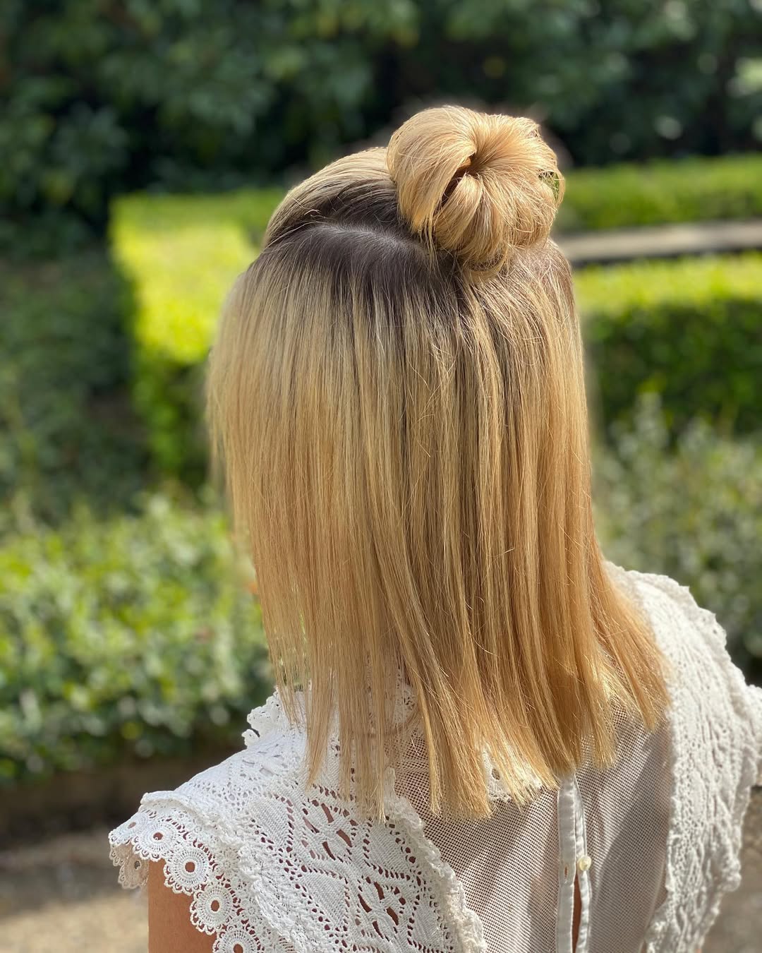 Chic Low Messy Bun: Simple Summer Hairstyles 2026 Woman with long, dark hair styled in a low, messy bun with face-framing pieces, perfect for simple summer hairstyles 2026. She wears a white eyelet top.