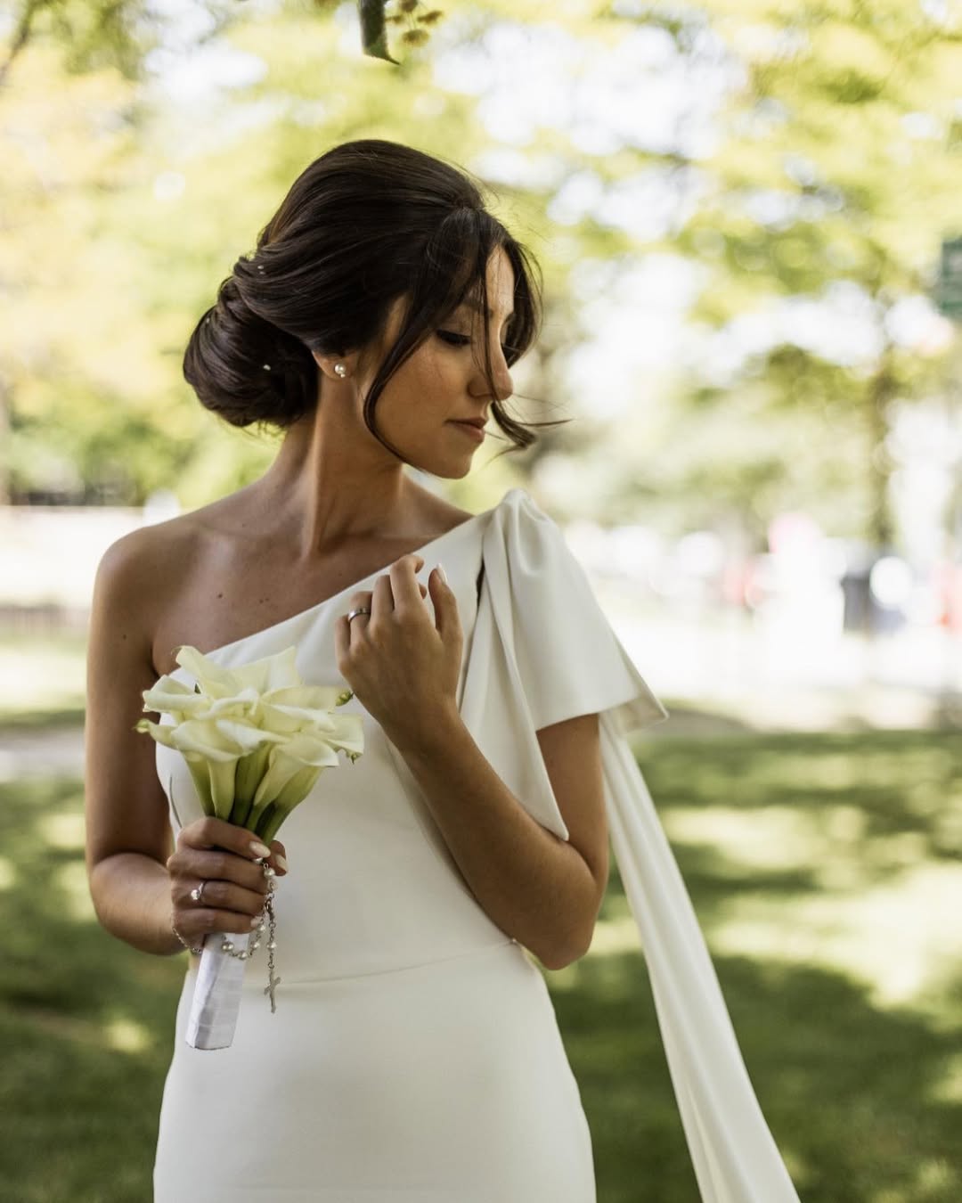 Beautiful summer bride hairstyles 2026 for an outdoor wedding, featuring a low bun with delicate white floral accents and loose face-framing curls.