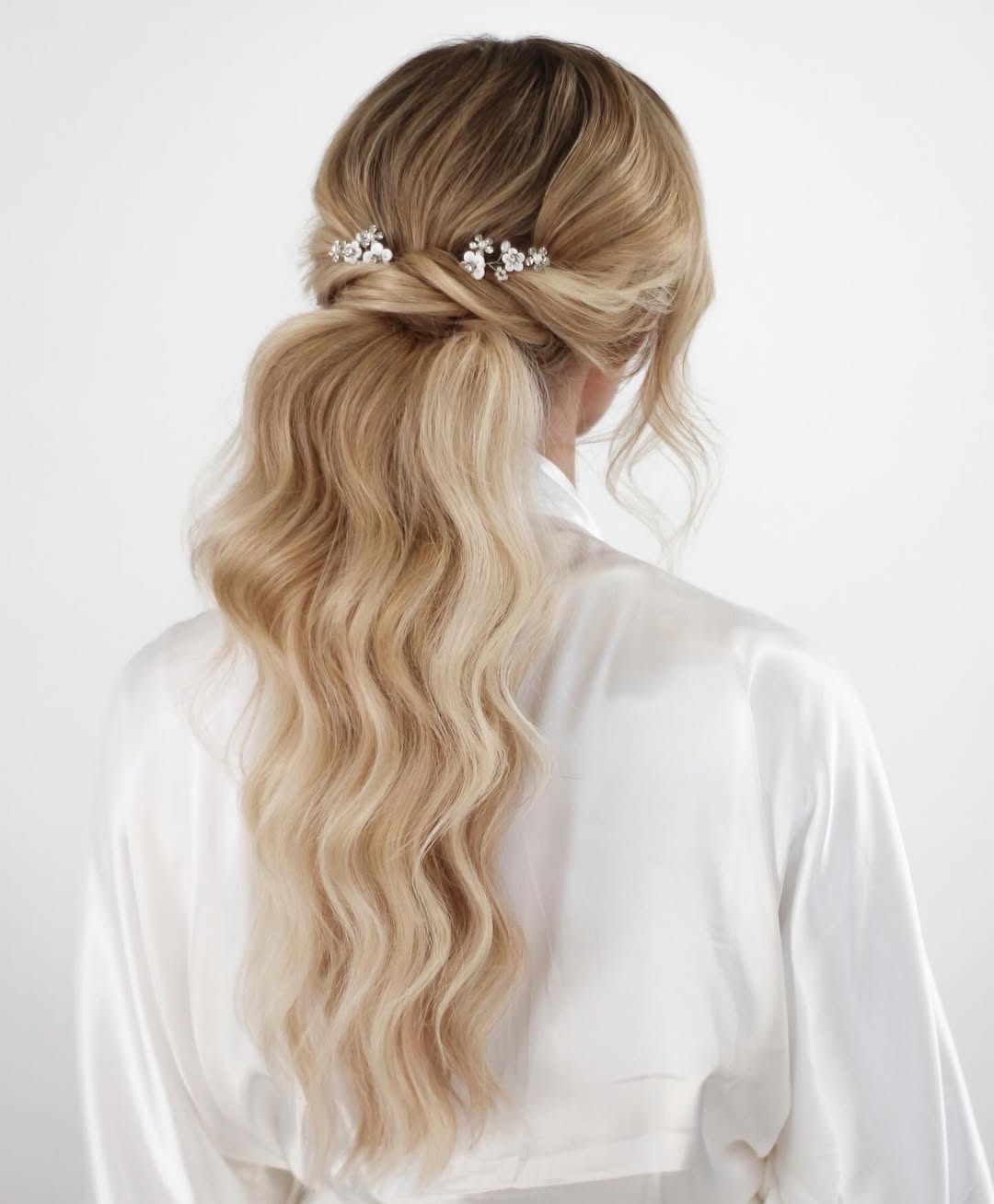 Elegant brunette bride with a twisted low bun and delicate floral hairpins, showcasing beautiful summer bride hairstyles 2026 for a sophisticated wedding.