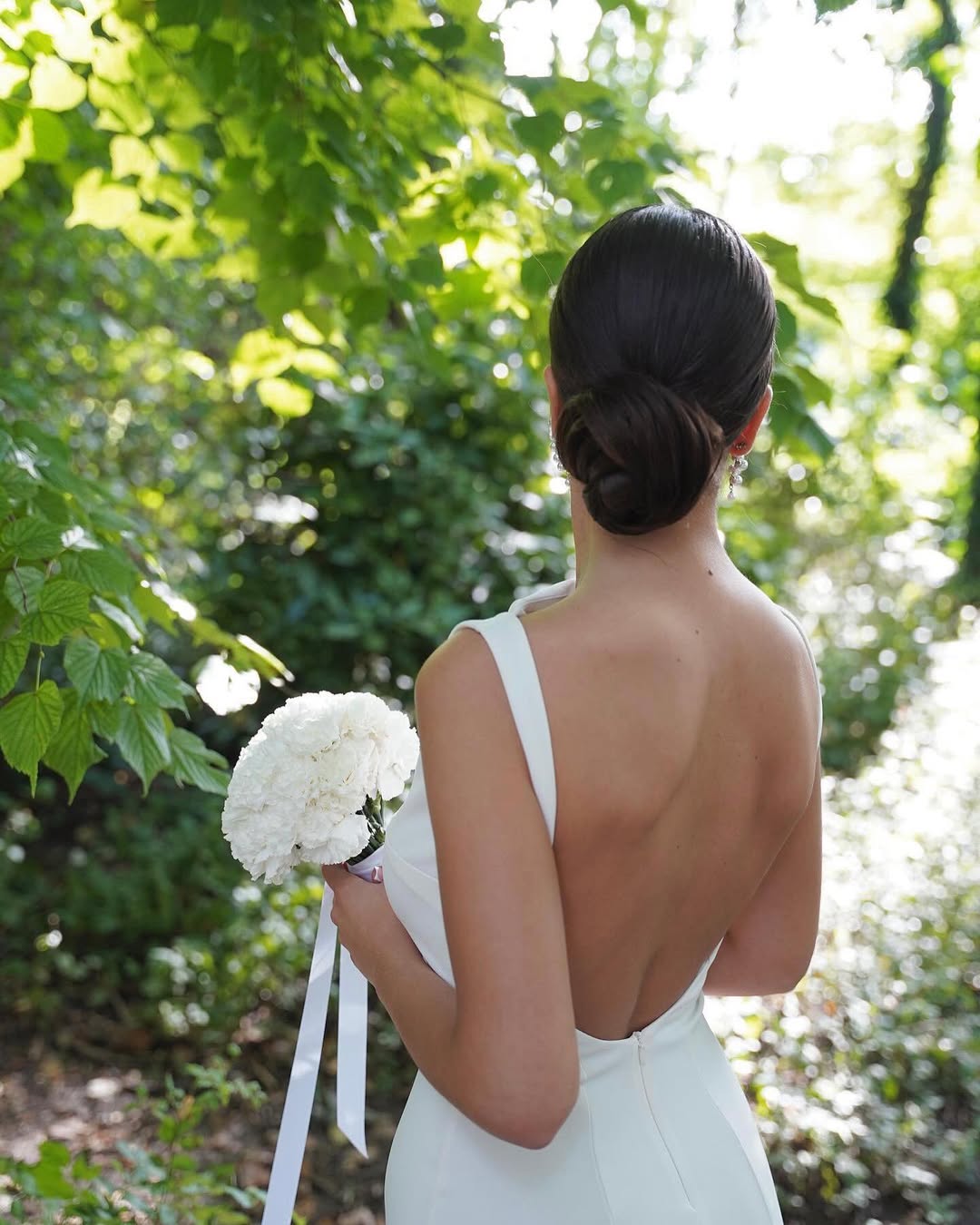 Elegant brunette bride showcasing a side-swept bun with delicate pearl hairpins, perfect for summer bride hairstyles 2026. A classic, sophisticated wedding day look.