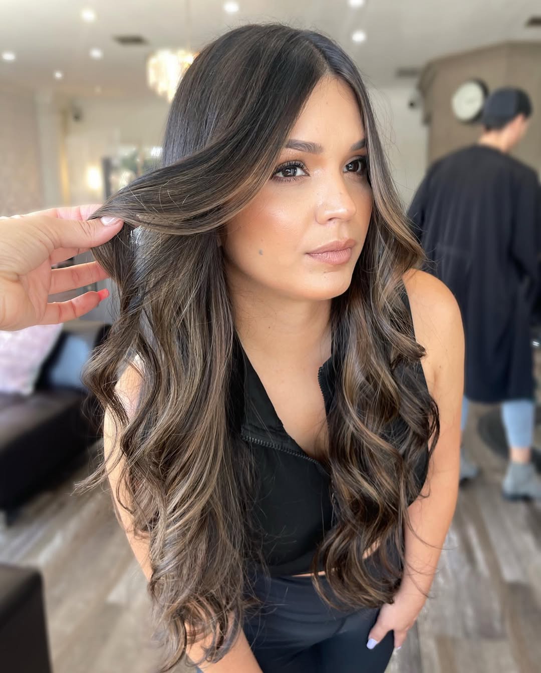 Beautiful woman with long, shiny dark hair styled in soft waves, perfect for summer dark hair looks 2026. She wears a flowy white dress in a sunlit outdoor setting, embodying effortless summer elegance.
