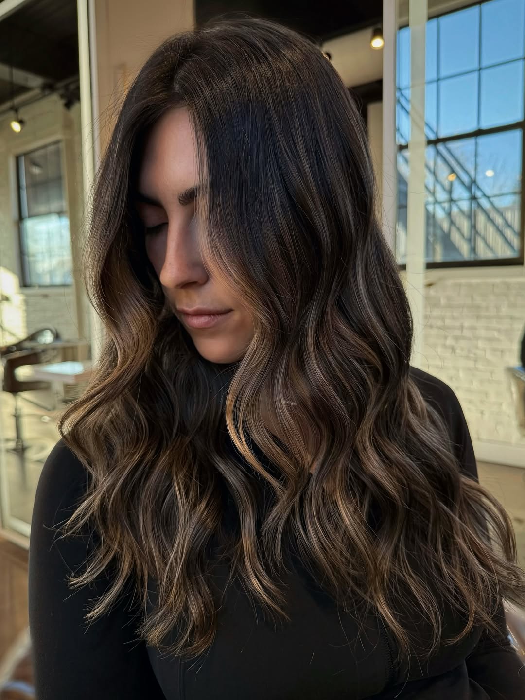 Beautiful woman with long, dark wavy hair styled in a chic, effortless look, perfect for summer dark hair looks 2026. She wears a casual white top, showcasing a natural, radiant aesthetic for warm weather.
