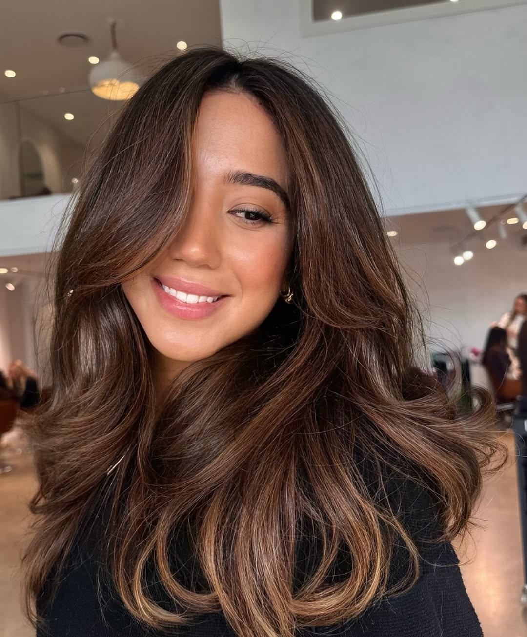 A woman with sleek, shiny dark hair styled in loose waves, paired with a vibrant red off-shoulder top for a chic summer look. Emphasizes summer dark hair looks 2026.