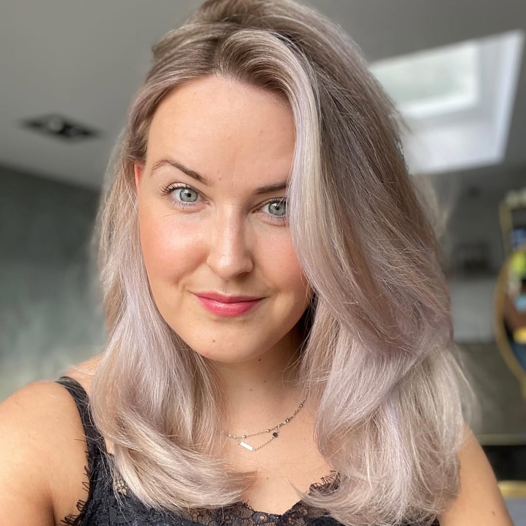 Close-up of a woman with vibrant caramel highlights and soft waves, showcasing a beautiful summer soft hair color 2026. Her hair shines in the sunlight.