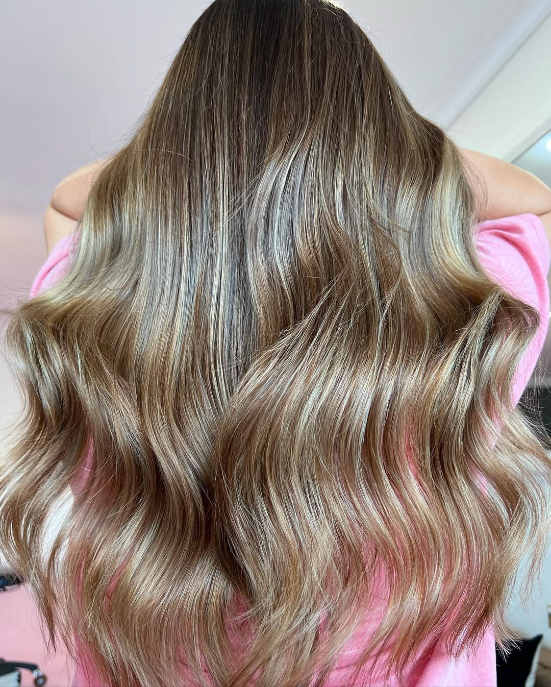 Woman smiling with sun-kissed blonde balayage, a popular summer soft hair color 2026, styled in loose waves, perfect for beach or casual outings.