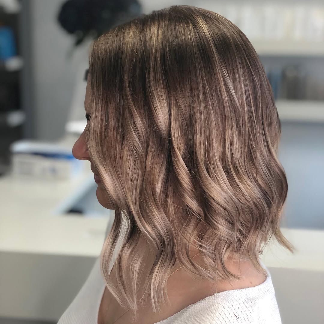 Close-up of a woman with warm, soft blonde hair, showcasing a beautiful summer soft hair color 2026. Her hair has subtle, sun-kissed highlights and natural waves, perfect for effortless summer style.
