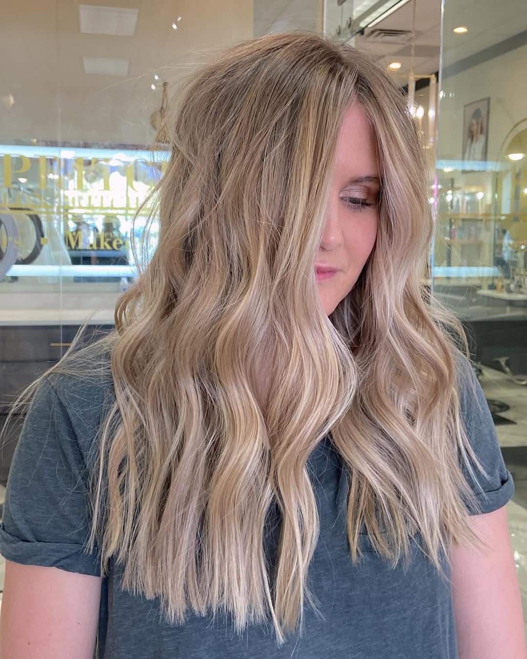 Beautiful woman with sunlit, flowing, warm blonde summer soft hair color 2026, smiling gently. The hair features natural-looking highlights and lowlights, perfectly complementing her glowing skin. Ideal for a chic casual outing.