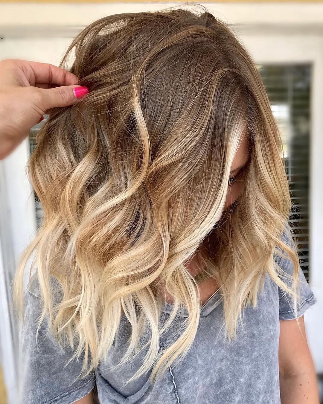 Close-up of a woman with natural waves showcasing beautiful summer soft hair color 2026, a blend of sun-kissed blonde and subtle caramel highlights.