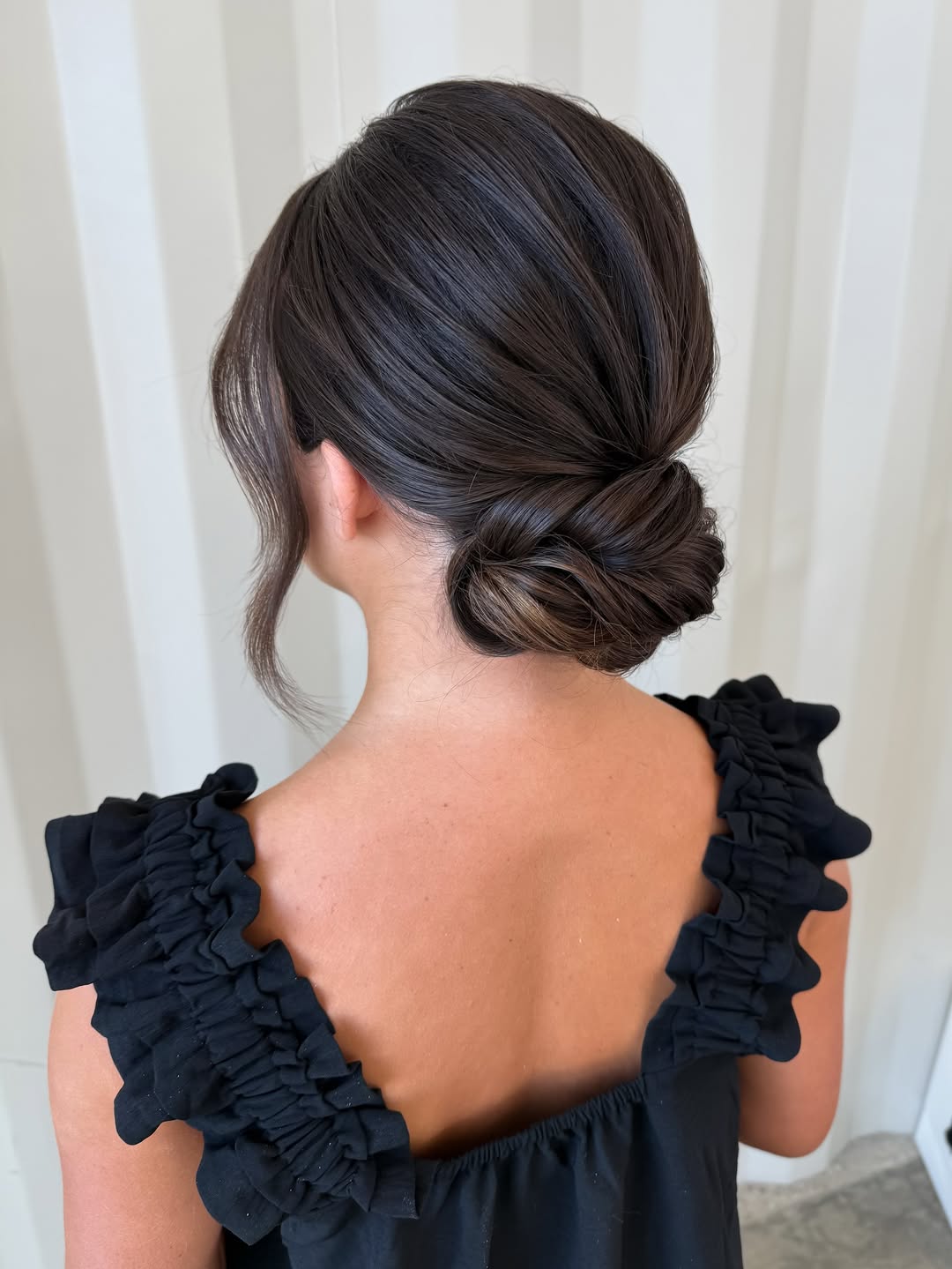 Elegant brunette woman with a loose, braided updo adorned with small white flowers, perfect for a summer wedding guest hairstyle 2026. Her hair is styled with soft waves around her face.