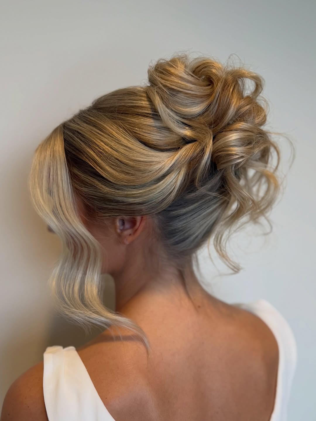 Elegant brunette woman with a loose, braided updo, adorned with delicate white flowers, perfect for a summer wedding guest hairstyle. Her hair complements a flowy pastel dress, ideal for an outdoor ceremony.