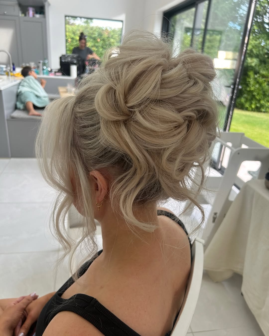 Elegant brunette woman with a loose, braided updo, perfect for a summer wedding guest hairstyle 2026. Her dark hair features soft waves and subtle highlights, complementing a formal outdoor event.