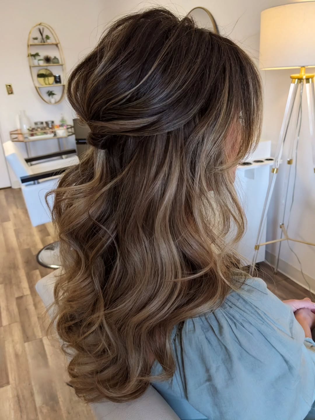 Elegant brunette woman with a loose, side-swept bun, adorned with delicate pearl pins, perfect summer wedding guest hairstyle 2026. Her hair is styled with soft waves framing her face, complementing a formal event.