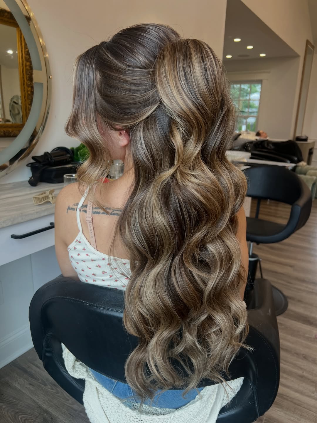Elegant brunette woman with a loose, low bun, featuring soft face-framing waves, perfect for a summer wedding guest hairstyle. This sophisticated updo offers a romantic touch for formal occasions.