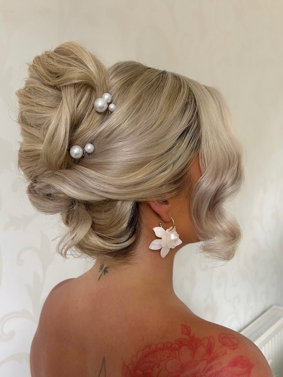 Beautiful blonde bride with a soft, romantic updo, featuring braided details and loose face-framing tendrils, perfect for summer wedding hairstyle ideas 2026. Her hair is adorned with delicate fresh flowers, creating an elegant and ethereal look for a garden wedding.