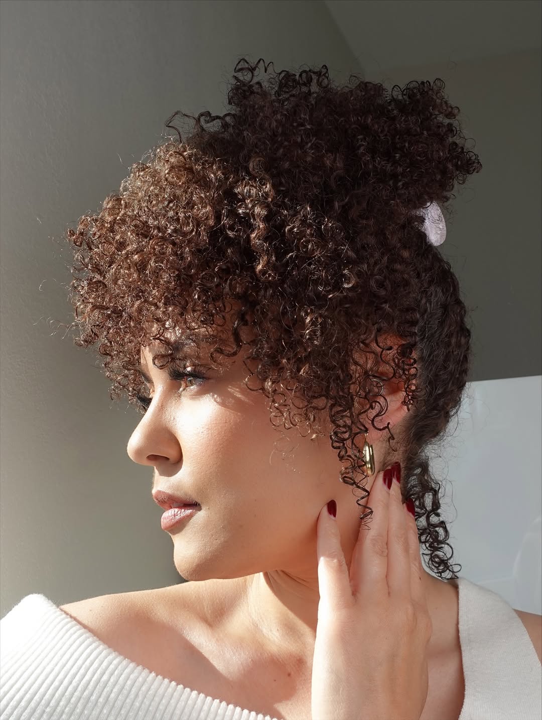 Close-up of a smiling woman with perfectly defined, bouncy blonde curls, showcasing radiant summer hair curly ideas 2026. Her hair has golden highlights that catch the light beautifully, framing her face.