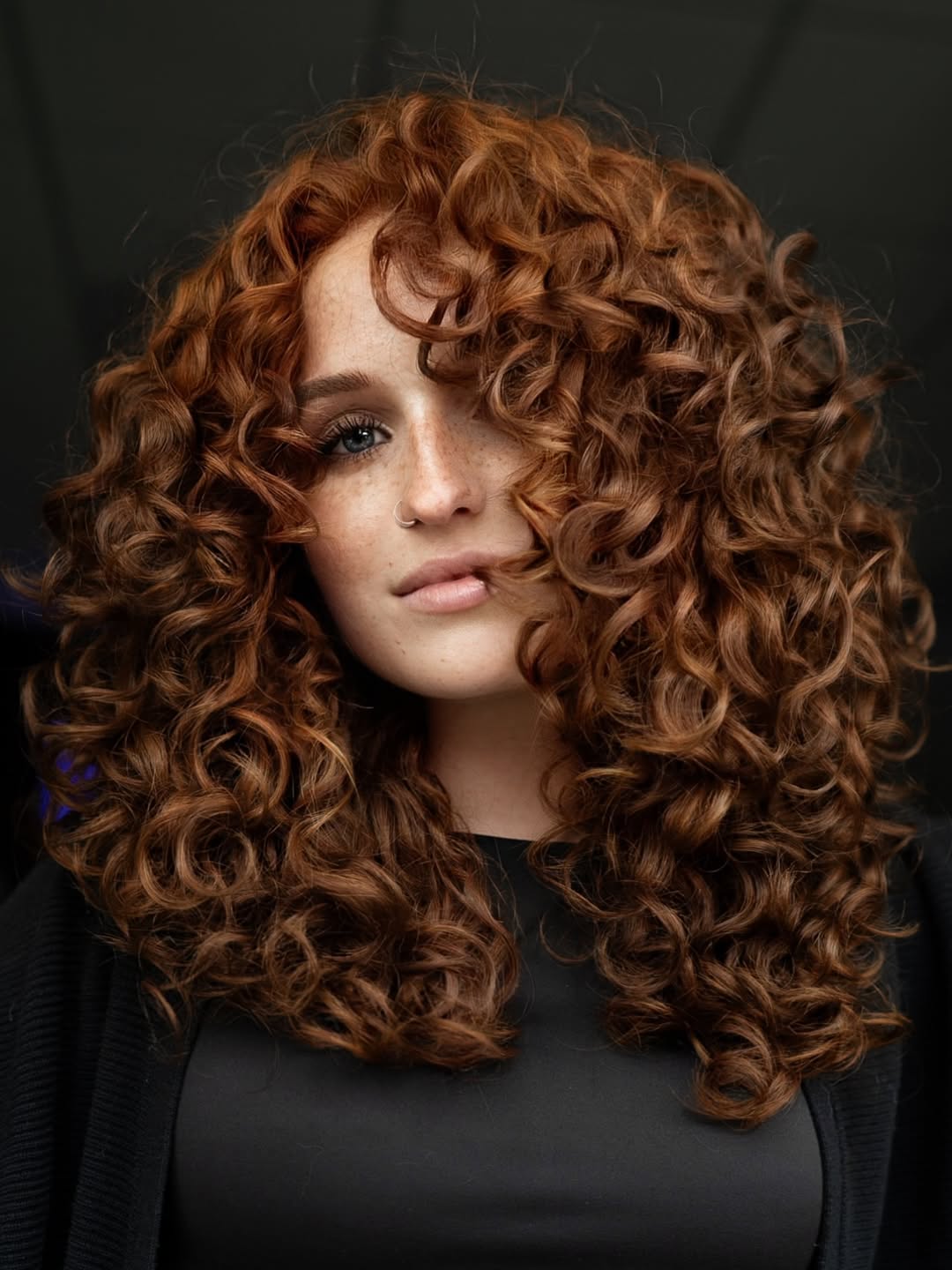 Close-up of a woman with bouncy, perfectly defined spirals showcasing stunning summer hair curly ideas 2026. Her long, dark curls are styled with volume and shine, perfect for a sunny day or evening out.