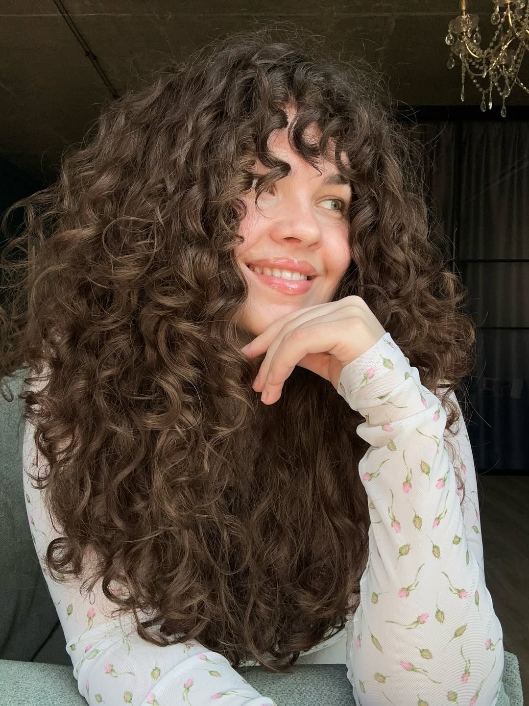 Close-up of a woman with vibrant, voluminious curly hair styled for summer. The brown, natural curls frame her face beautifully, showcasing a playful and effortless look, perfect for summer hair curly ideas 2026.