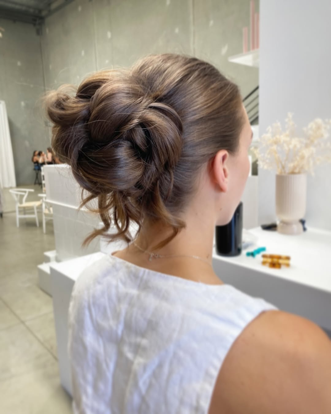 Blonde woman with a braided bun updo for summer, wearing a floral top, perfect for warm weather and beach days. This chic style is a fantastic summer hair updo.