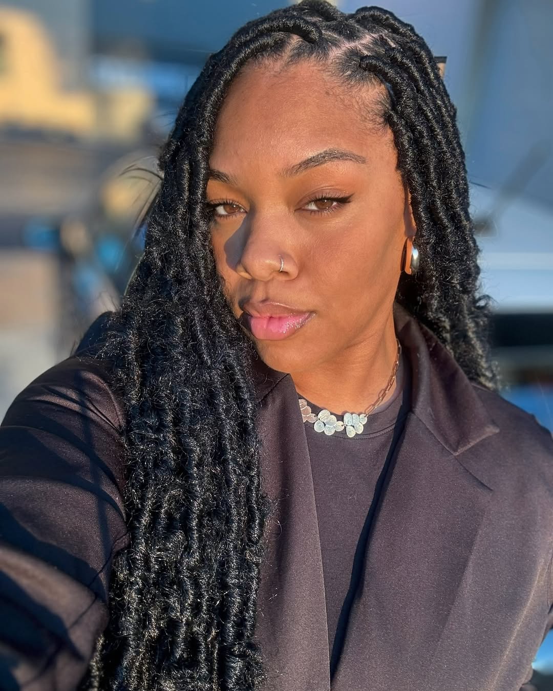Close-up of a Black woman with vibrant, long fuchsia pink braids, styled into a high half-up half-down top knot, showcasing a trendy summer hairstyle. This look is perfect for a festival.