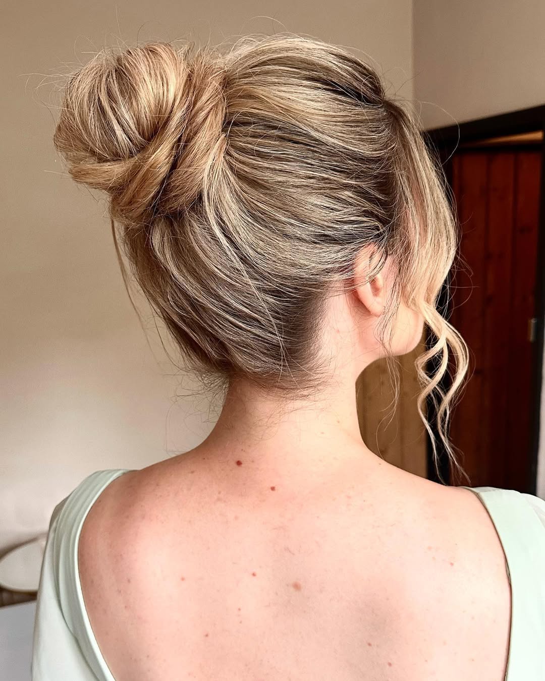 Blonde woman with a braided ponytail, her summer hairstyle hot weather ready. She's outdoors, wearing a white sleeveless top with a denim jacket.