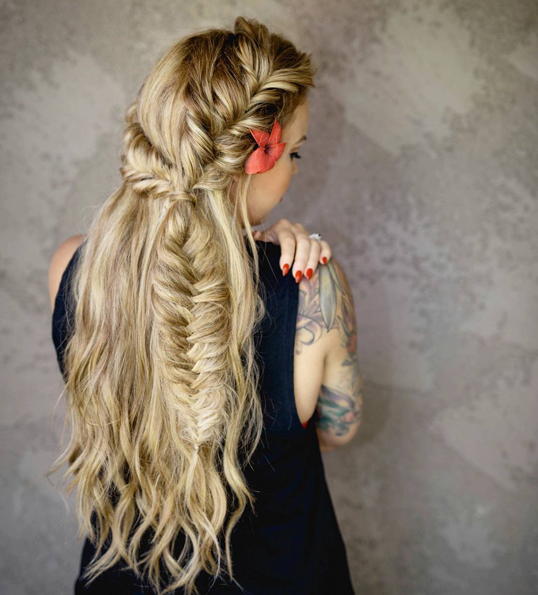 Blonde woman with long hair in a stylish high ponytail, a perfect summer hairstyle for hot weather, wearing a white sleeveless top outdoors.