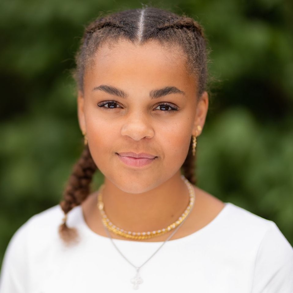 Chic Half-Up Bun for Teen Hairstyles Summer 2026 Close-up of a teen girl with long, wavy blonde hair styled in a half-up messy bun with face-framing tendrils, perfect for teen hairstyles summer 2026. She wears a casual white t-shirt, glowing with natural light.