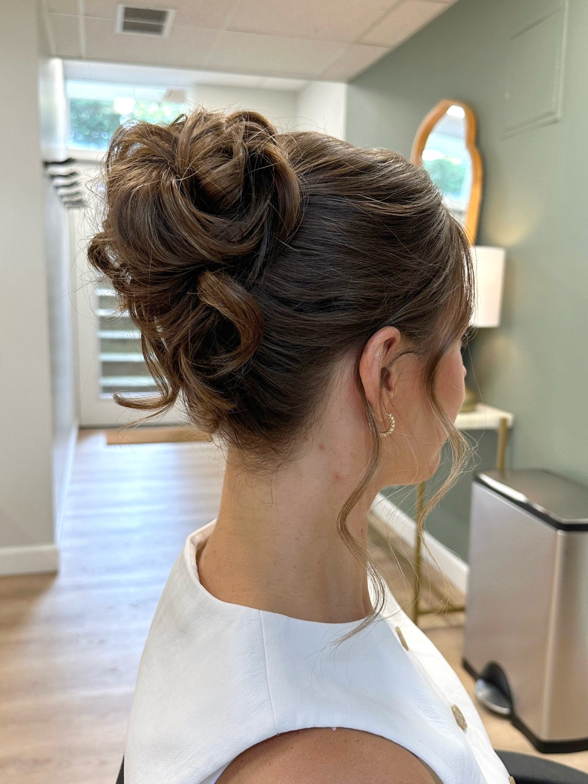 Messy Romantic High Bun With Face Framing Tendrils